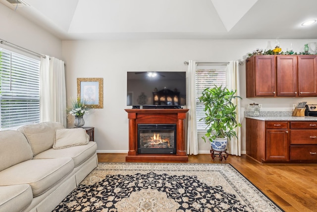 living area featuring light wood-style floors, vaulted ceiling, and a glass covered fireplace