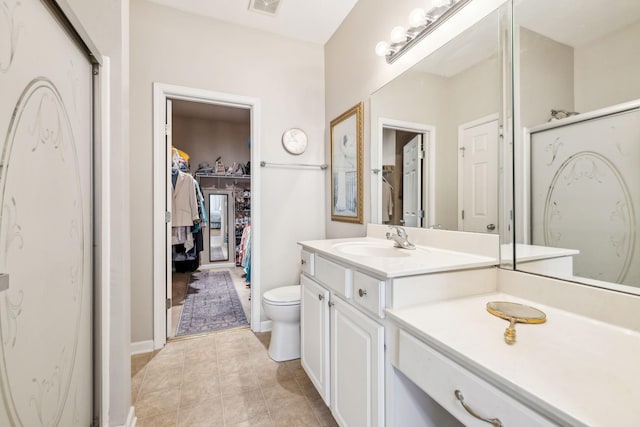 bathroom featuring vanity, toilet, tile patterned floors, a walk in closet, and a shower with door