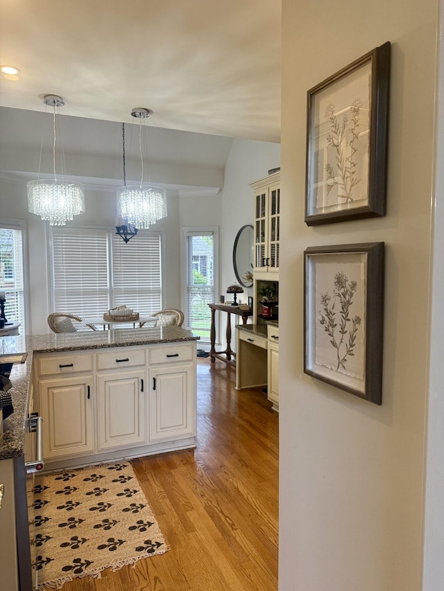 kitchen featuring light wood-style flooring, a chandelier, pendant lighting, white cabinetry, and lofted ceiling