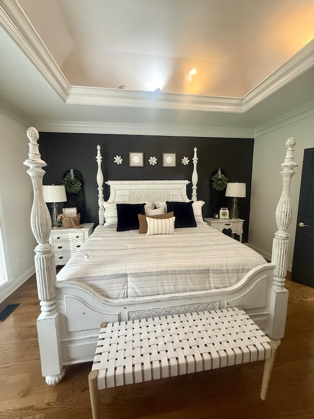 bedroom featuring a raised ceiling, ornamental molding, wood finished floors, and baseboards