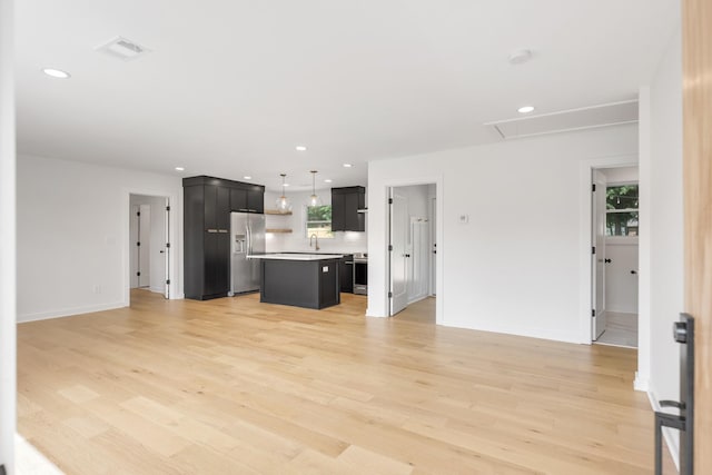 unfurnished living room featuring attic access, light wood finished floors, recessed lighting, a sink, and baseboards