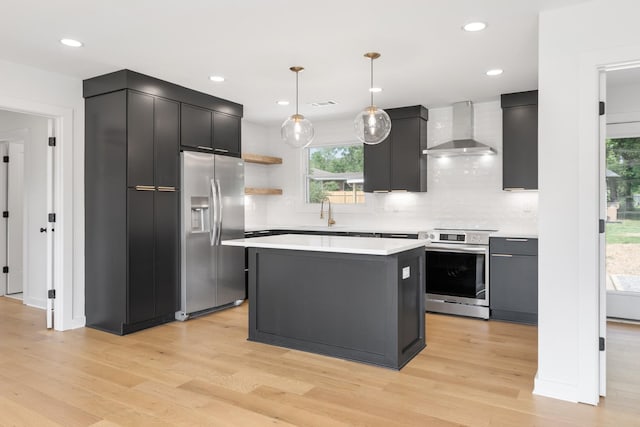 kitchen featuring stainless steel appliances, wall chimney exhaust hood, light wood-type flooring, light countertops, and tasteful backsplash