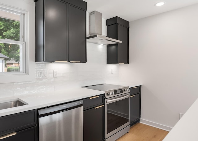 kitchen with appliances with stainless steel finishes, wall chimney exhaust hood, backsplash, light countertops, and light wood-style floors
