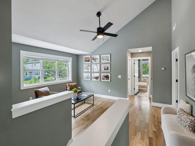 living area featuring high vaulted ceiling, ceiling fan, light wood-type flooring, and baseboards
