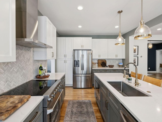 kitchen with appliances with stainless steel finishes, a sink, wall chimney exhaust hood, backsplash, and white cabinetry