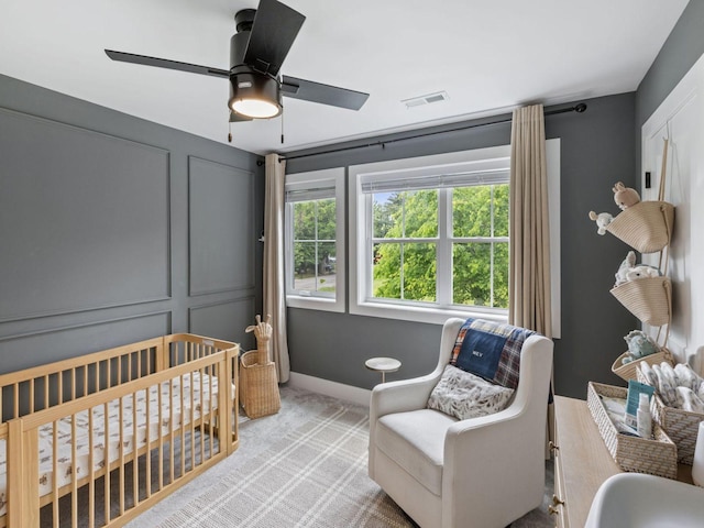 bedroom with multiple windows, light carpet, a crib, and ceiling fan
