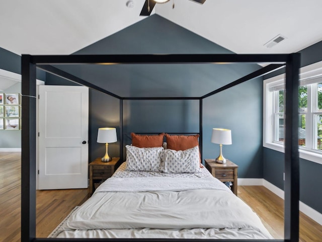bedroom with vaulted ceiling, wood finished floors, and baseboards
