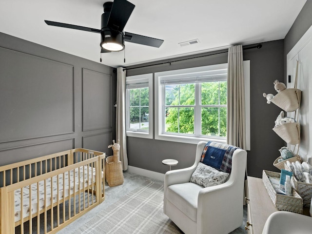 bedroom with a crib, light carpet, ceiling fan, baseboards, and a decorative wall