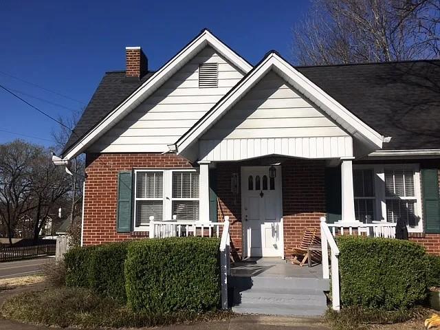 bungalow-style home featuring brick siding, covered porch, and a chimney