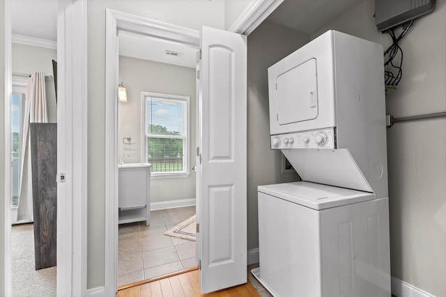clothes washing area with estacked washer and dryer, baseboards, light wood-style flooring, and crown molding