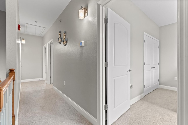 corridor with attic access, light colored carpet, and baseboards