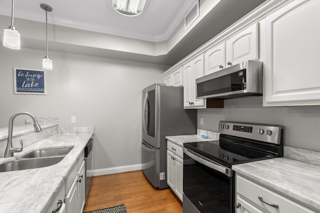 kitchen featuring appliances with stainless steel finishes, a sink, white cabinets, light wood-style floors, and ornamental molding