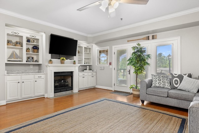 living room with a ceiling fan, wood finished floors, crown molding, plenty of natural light, and a fireplace with flush hearth