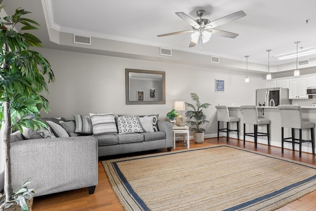 living room with wood finished floors, a ceiling fan, and crown molding