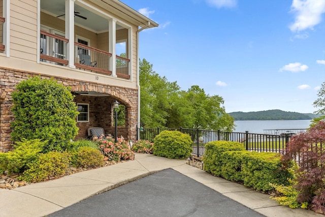 view of patio with a balcony, fence, a ceiling fan, and a water view