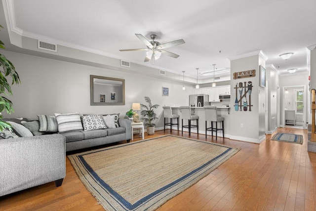 living room with ceiling fan, hardwood / wood-style flooring, ornamental molding, and baseboards