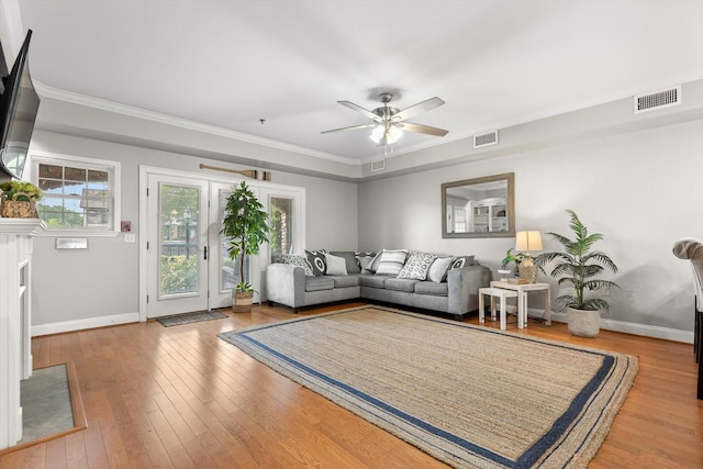 living area with baseboards, wood-type flooring, ceiling fan, and crown molding