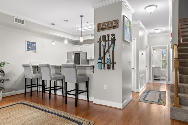kitchen featuring stainless steel fridge with ice dispenser, a breakfast bar, hardwood / wood-style floors, white cabinets, and baseboards