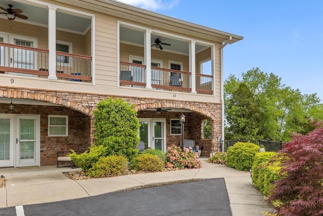 view of front of home with a balcony, a ceiling fan, stone siding, fence, and a patio