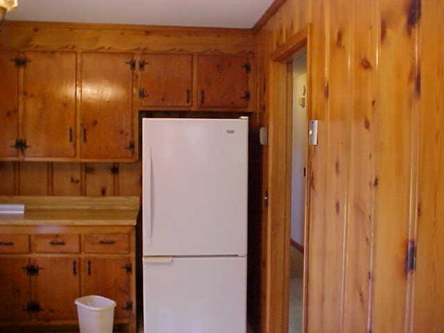 kitchen with freestanding refrigerator, brown cabinetry, light countertops, and wood walls