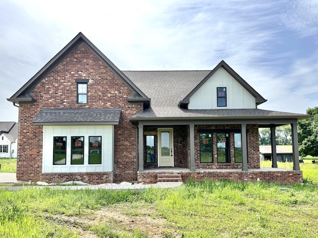 view of front of home featuring brick siding, covered porch, board and batten siding, and roof with shingles