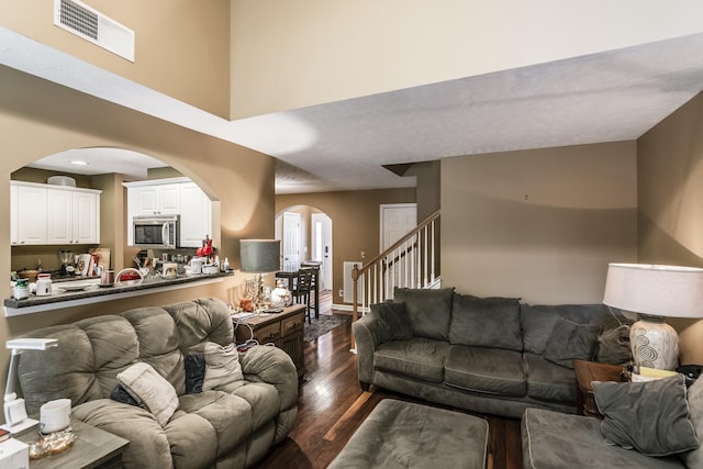 living room featuring arched walkways, dark wood-style floors, stairway, and a high ceiling