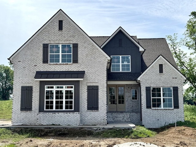 view of front of house featuring board and batten siding, french doors, brick siding, and roof with shingles