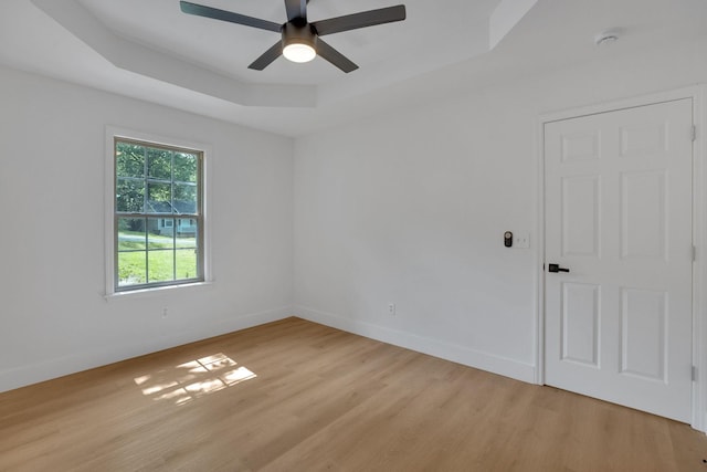 spare room with a tray ceiling, light wood finished floors, a ceiling fan, and baseboards