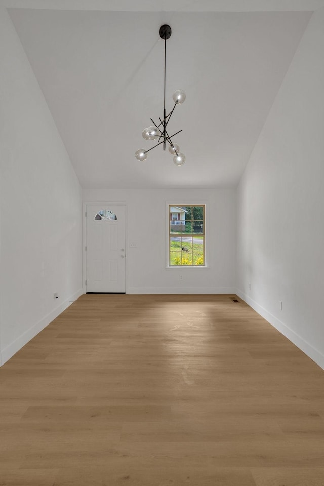 unfurnished living room featuring a chandelier, light wood-type flooring, and baseboards