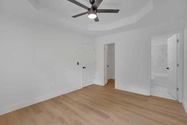 unfurnished bedroom featuring baseboards, a raised ceiling, light wood-style flooring, and ensuite bath