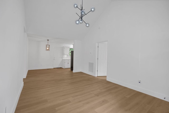 unfurnished living room with high vaulted ceiling, a chandelier, light wood-type flooring, and baseboards