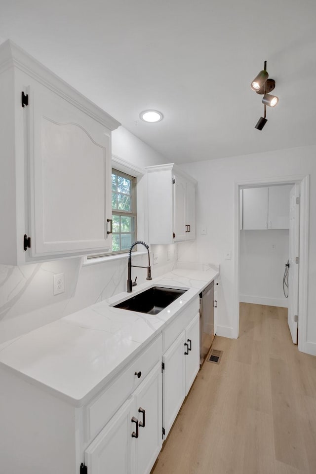 kitchen featuring a sink, stainless steel dishwasher, light wood-type flooring, white cabinets, and baseboards