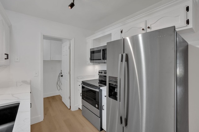 kitchen featuring stainless steel appliances, light wood-style floors, white cabinets, light stone counters, and baseboards