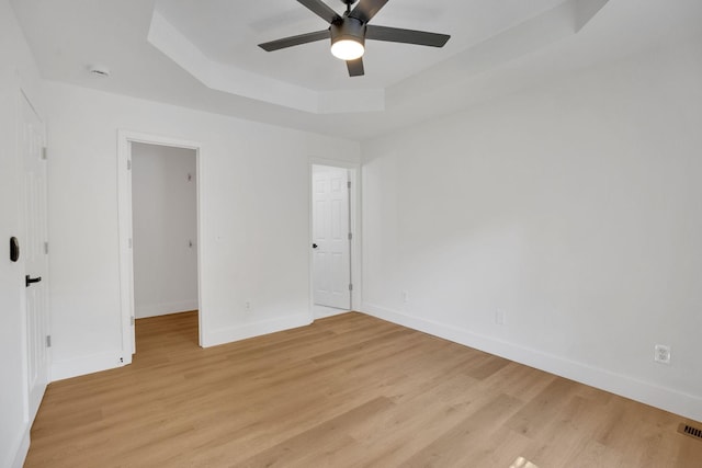 unfurnished bedroom featuring a raised ceiling, baseboards, light wood-style flooring, and a spacious closet