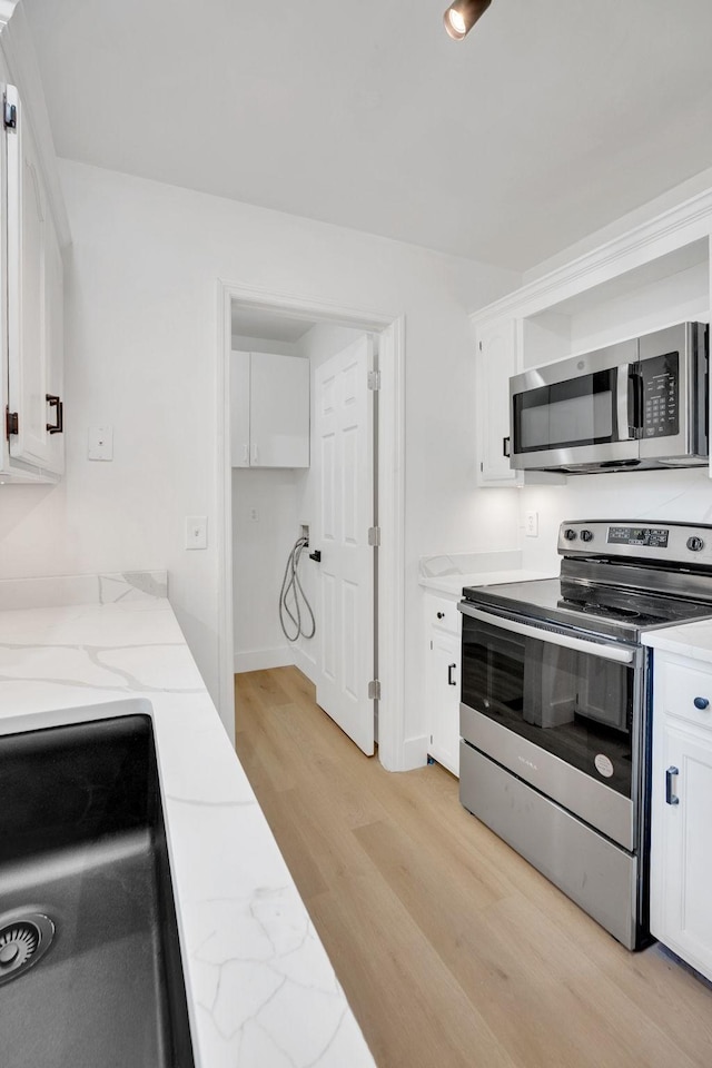 kitchen featuring stainless steel appliances, light wood-style floors, white cabinetry, light stone counters, and baseboards