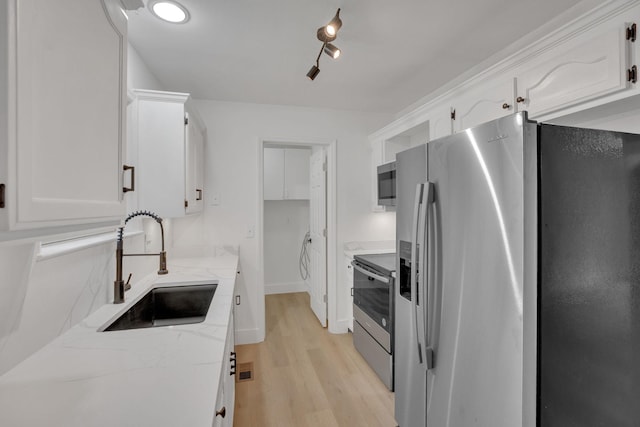 kitchen featuring appliances with stainless steel finishes, a sink, light wood-type flooring, light stone counters, and white cabinetry