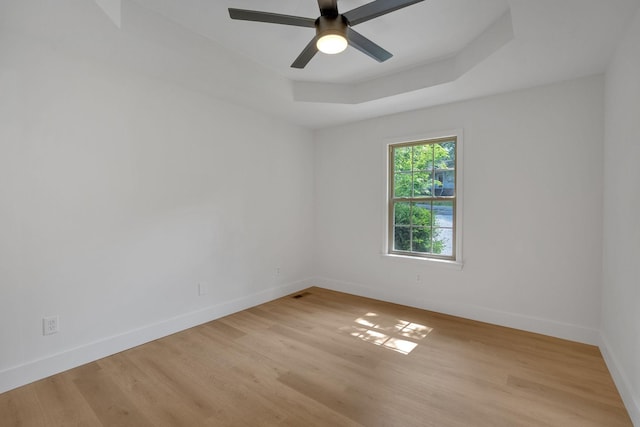 spare room featuring light wood-type flooring, baseboards, ceiling fan, and a raised ceiling