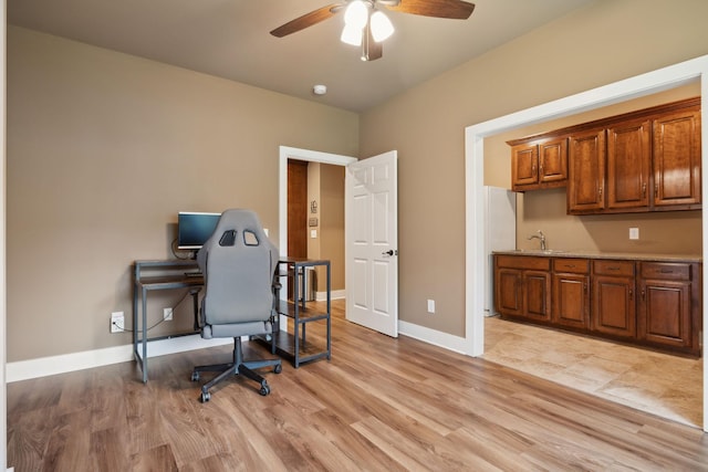 office space with a ceiling fan, a sink, light wood-style flooring, and baseboards