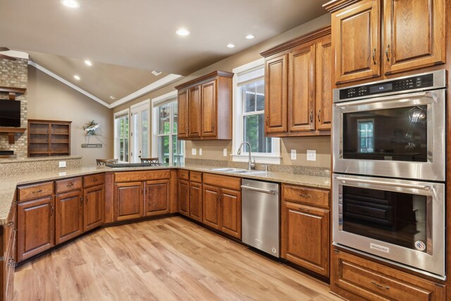 kitchen with stainless steel appliances, a sink, brown cabinets, vaulted ceiling, and light wood finished floors