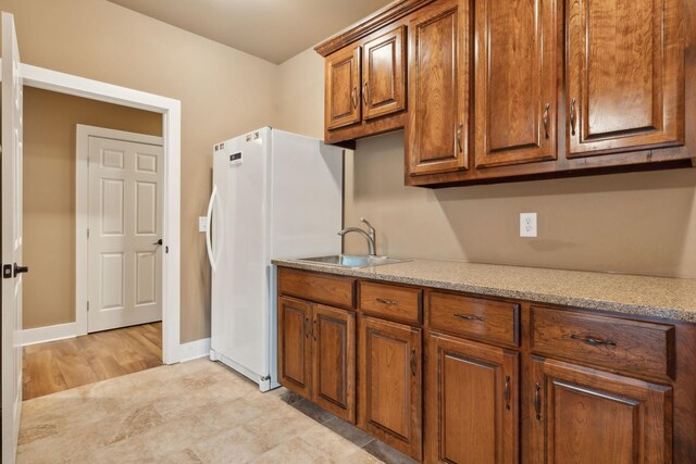 kitchen with freestanding refrigerator, a sink, brown cabinets, and baseboards