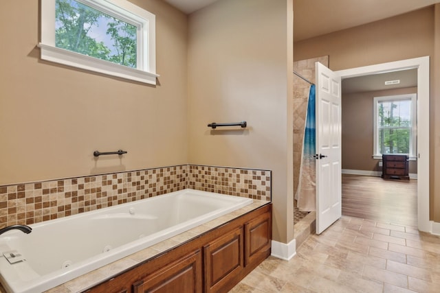 full bathroom featuring a jetted tub, a tile shower, and baseboards