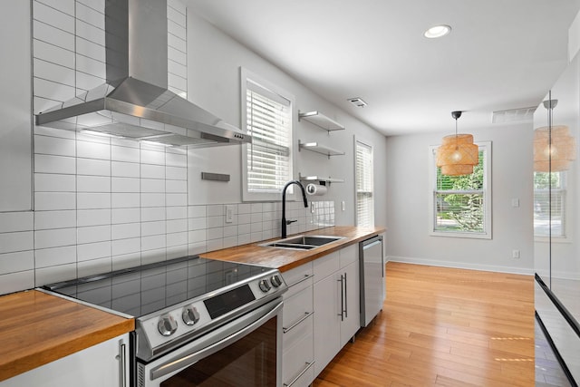 kitchen featuring wood counters, appliances with stainless steel finishes, open shelves, wall chimney range hood, and recessed lighting