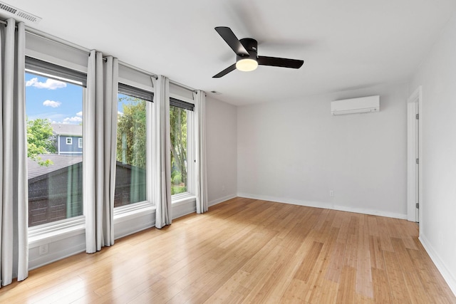 empty room with a wall mounted air conditioner, light wood-style flooring, baseboards, and a ceiling fan