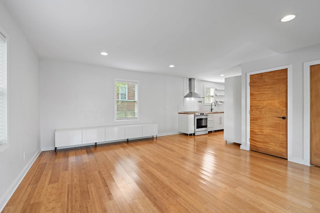unfurnished living room with light wood finished floors, recessed lighting, baseboards, and a sink