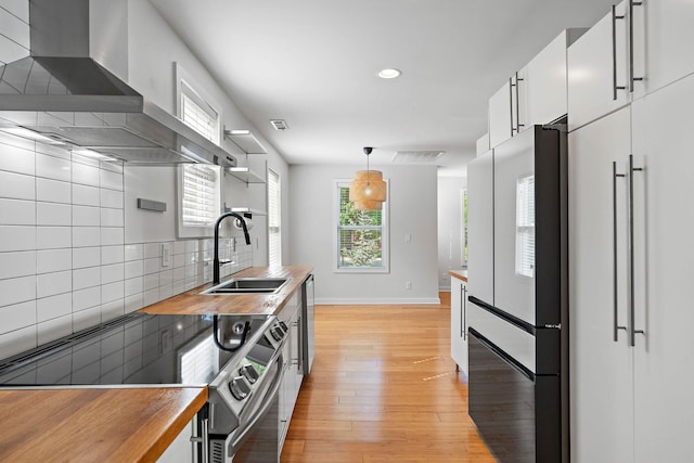 kitchen with wall chimney exhaust hood, butcher block counters, a sink, range with electric stovetop, and open shelves