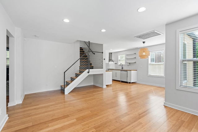unfurnished living room with stairway, recessed lighting, baseboards, light wood finished floors, and a sink