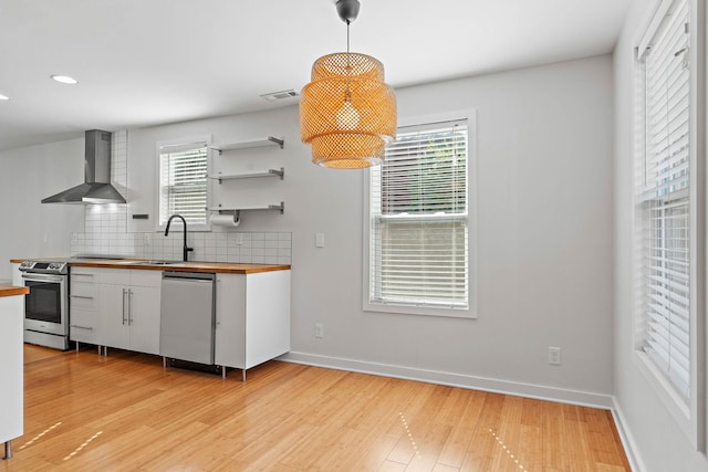kitchen featuring wall chimney range hood, wood counters, a sink, appliances with stainless steel finishes, and white cabinets