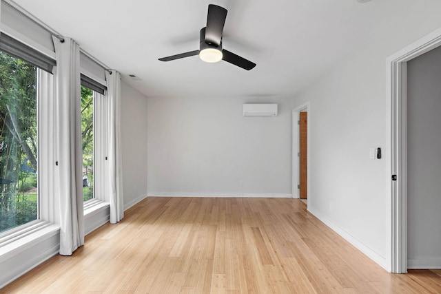 spare room featuring a wall unit AC, light wood-style flooring, a ceiling fan, and baseboards