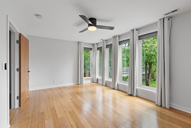 empty room with plenty of natural light, ceiling fan, baseboards, and light wood-style floors