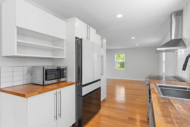 kitchen with butcher block countertops, stainless steel microwave, freestanding refrigerator, wall chimney exhaust hood, and recessed lighting